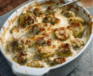 Delicious creamy baked Brussels sprouts served on a white plate, garnished with herbs.