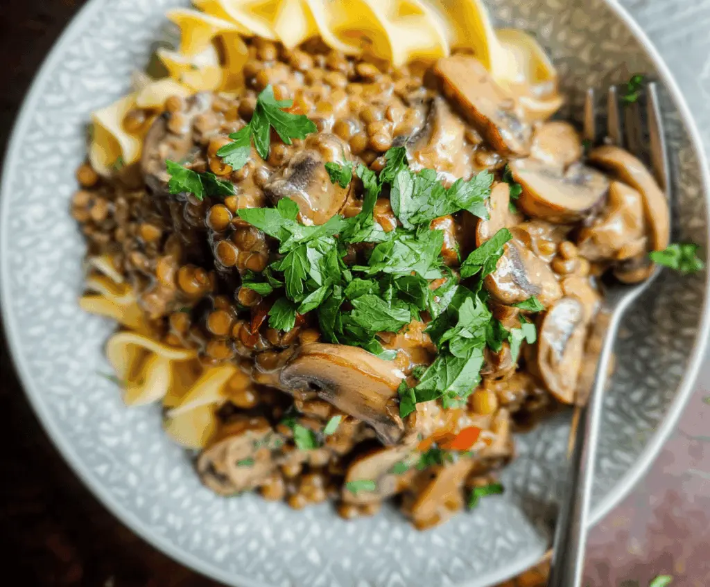 Creamy Lentil Mushroom Stroganoff served in a bowl with fresh herbs, featuring tender lentils, sautéed mushrooms, and a rich sauce, perfect for a hearty vegetarian meal.